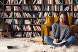 Young female Word Boutique style writer in library indoors working sitting on the carpet taking notes in organizer for book thoughtful concentrated